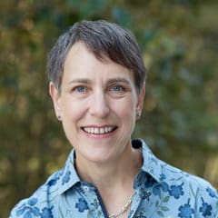 Smiling person outdoors with short hair.