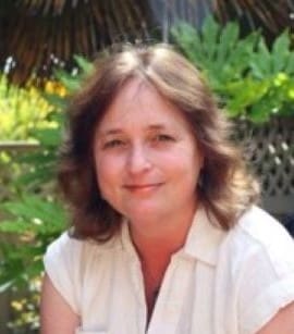 Woman smiling outdoors with green foliage background.