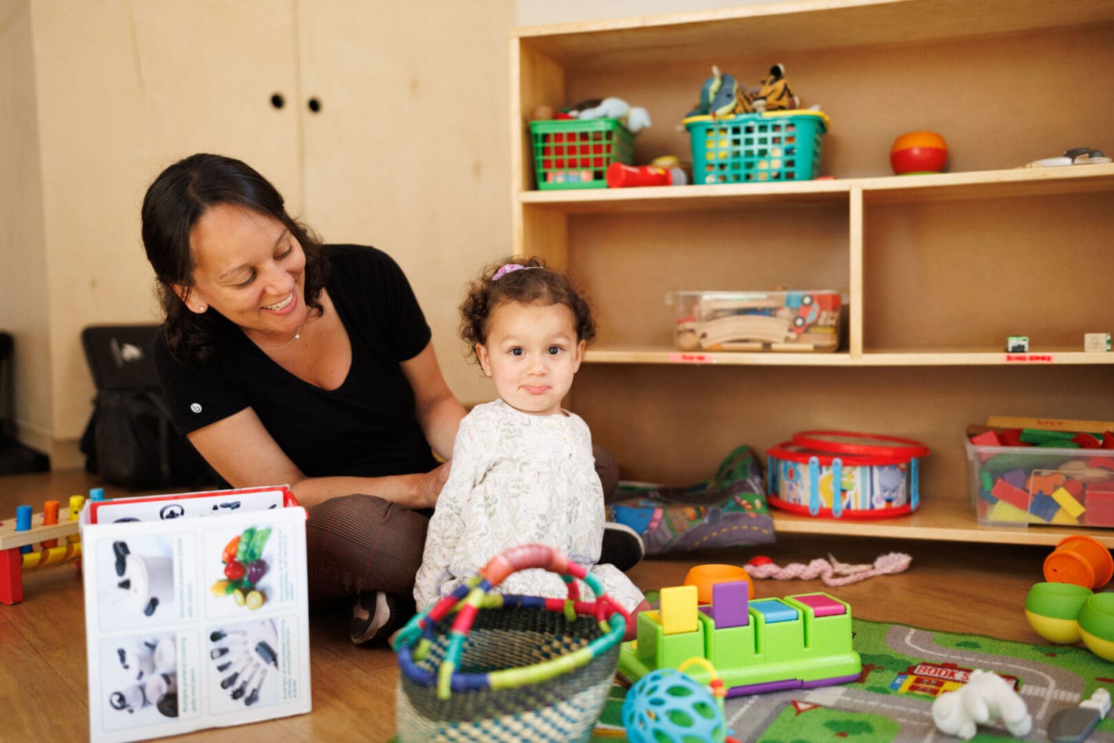 Woman and child playing in toy-filled room.