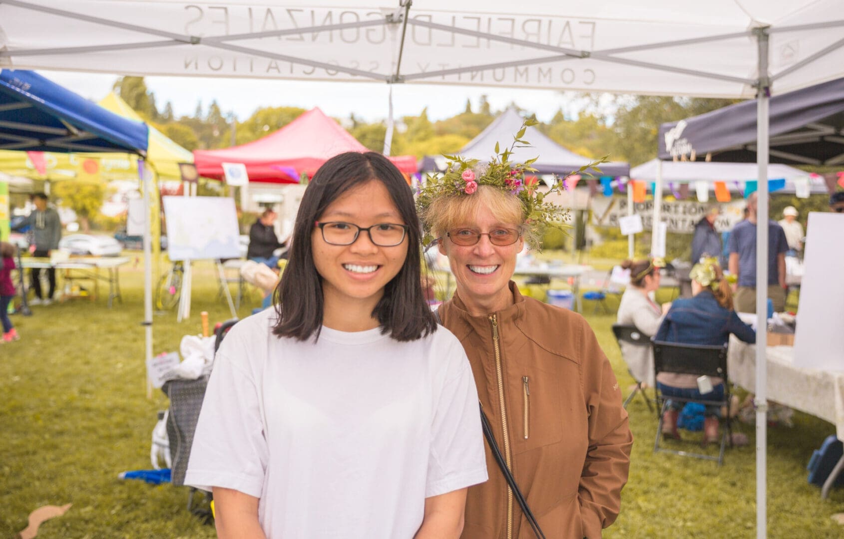 Two women smiling at outdoor market.