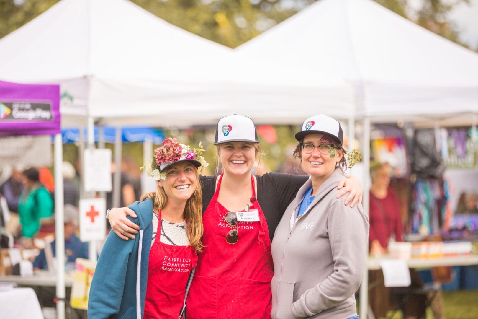 Three people smiling at outdoor market.